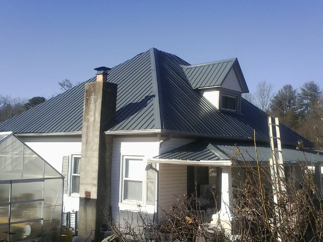 Dark blue standing seam metal roof on a white farmhouse with dormer — Slate & Tile Roof Repair by Roofing Brothers in Avenue