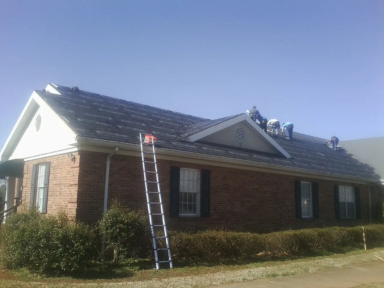 Crew tearing shingles off a brick ranch roof with a ladder set — Emergency Roof Repair work by our crew in Avenue