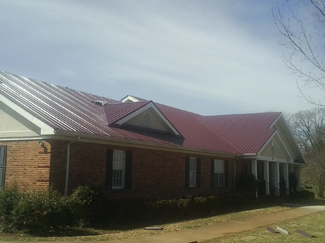 Red metal roof with gabled entries on a long brick building, from a Hail Damage Roof Repair job in Avenue