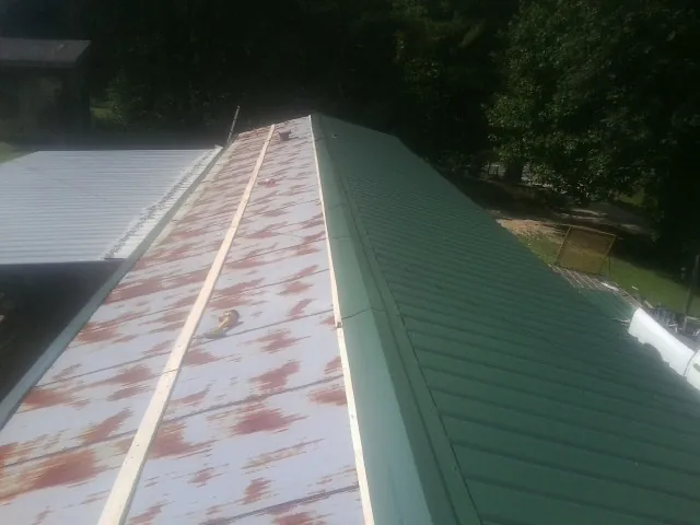 Old rusted panels beside newly installed green metal roofing — Wind Damage Roof Repair by Roofing Brothers in Avenue