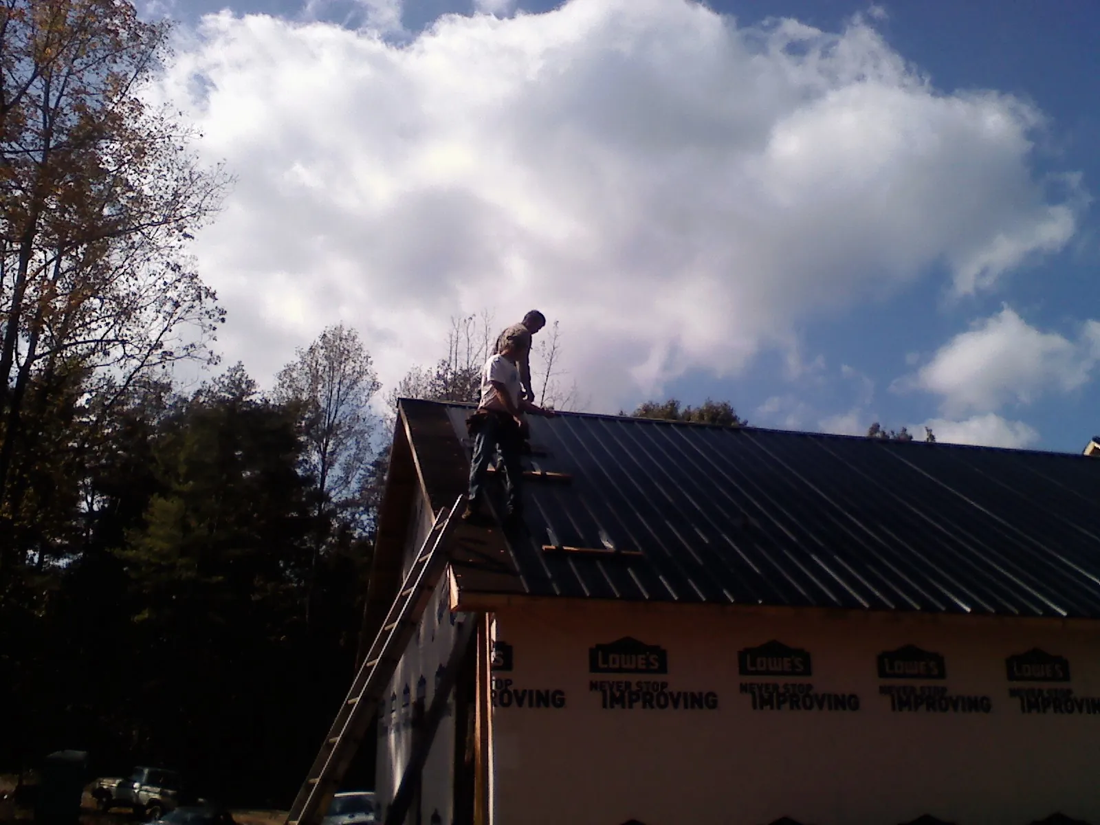 Roofer fastening dark metal panels high against a cloudy sky, from a Roof Inspection job in Avenue