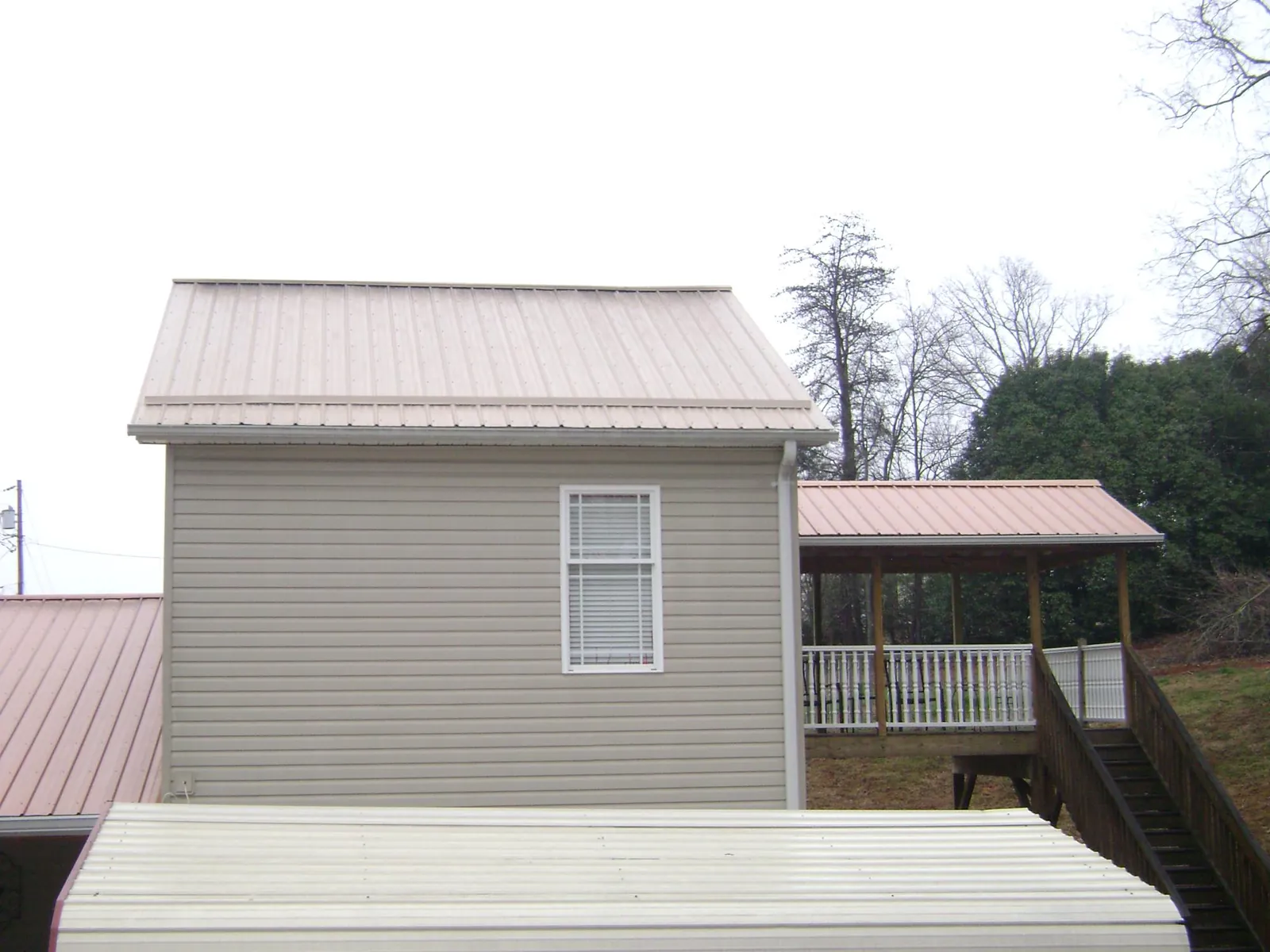 Tan metal roofs on a two story addition and attached porch, from a Roof Replacement job in Avenue